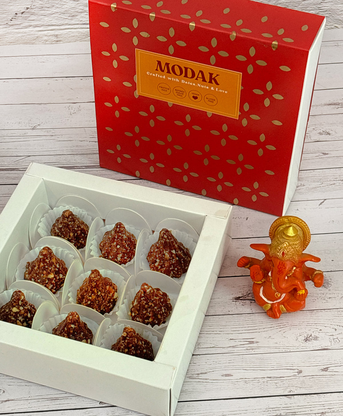 Gift set with Modak, Ganesh Chaturthi items, and a yellow ribbon on a wooden surface. Ganesh Chaturthi. Gifting. Made in Small Batches. Deliciously Decadent. Vegan Gluten Free Refined Sugar Free. Delicious Modak. Nuts. Delivery throughout U.A.E. HeartiGrub