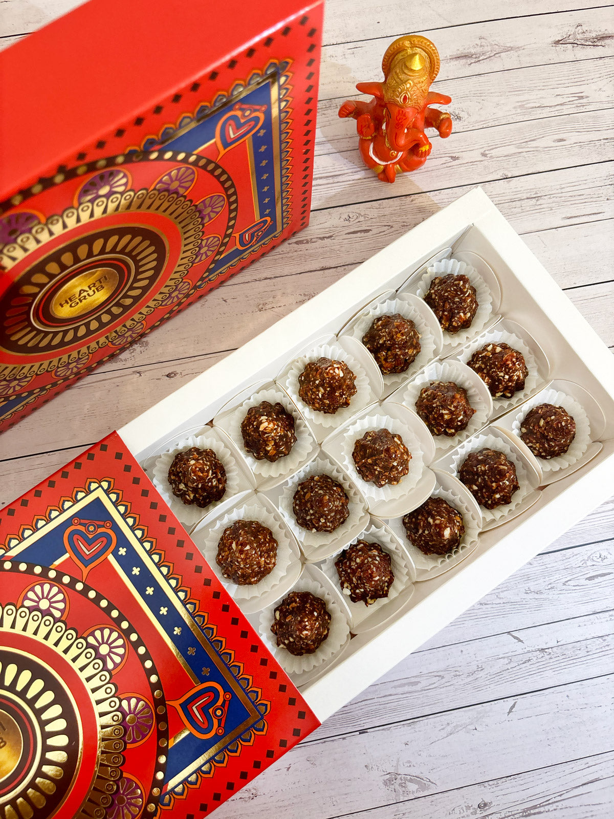 Gift set with Modak, Ganesh Chaturthi items, and a yellow ribbon on a wooden surface. Ganesh Chaturthi. Gifting. Made in Small Batches. Deliciously Decadent. Vegan Gluten Free Refined Sugar Free. Delicious Modak. Nuts. Delivery throughout U.A.E. HeartiGrub