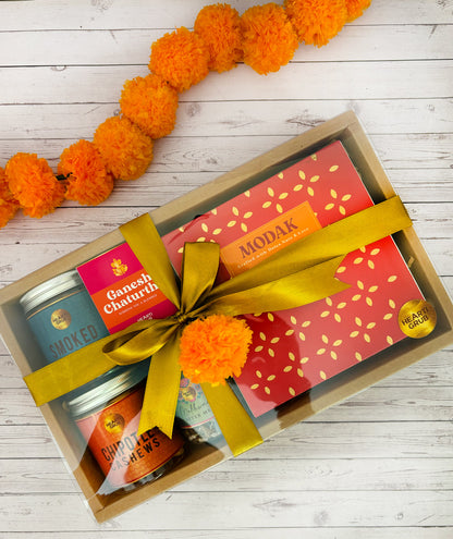 Gift set with Modak, Ganesh Chaturthi items, and a yellow ribbon on a wooden surface. Ganesh Chaturthi. Gifting. Made in Small Batches. Deliciously Decadent. Vegan Gluten Free Refined Sugar Free. Delicious Modak. Nuts. Delivery throughout U.A.E.