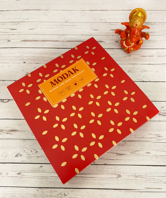 Gift set with Modak, Ganesh Chaturthi items, and a yellow ribbon on a wooden surface. Ganesh Chaturthi. Gifting. Made in Small Batches. Deliciously Decadent. Vegan Gluten Free Refined Sugar Free. Delicious Modak. Nuts. Delivery throughout U.A.E. HeartiGrub