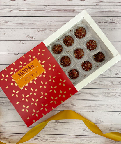 Gift set with Modak, Ganesh Chaturthi items, and a yellow ribbon on a wooden surface. Ganesh Chaturthi. Gifting. Made in Small Batches. Deliciously Decadent. Vegan Gluten Free Refined Sugar Free. Delicious Modak. Nuts. Delivery throughout U.A.E. HeartiGrub