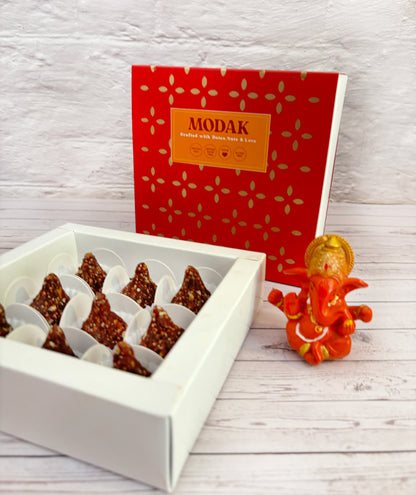 Gift set with Modak, Ganesh Chaturthi items, and a yellow ribbon on a wooden surface. Ganesh Chaturthi. Gifting. Made in Small Batches. Deliciously Decadent. Vegan Gluten Free Refined Sugar Free. Delicious Modak. Nuts. Delivery throughout U.A.E. HeartiGrub