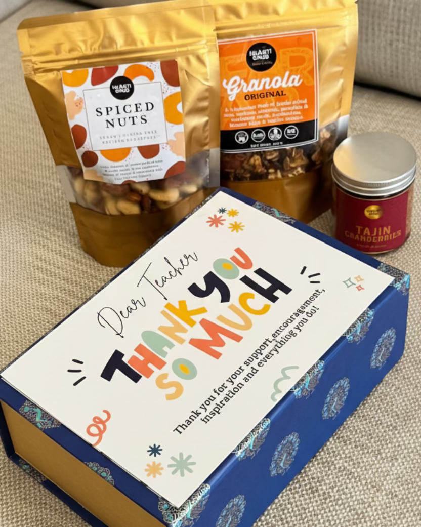 Box with 'Thank you so much' message, granola, spiced nuts, and a jar on a textured surface. HeartiGrub Gift Hamper. Teachers Day. Delivery in UAE