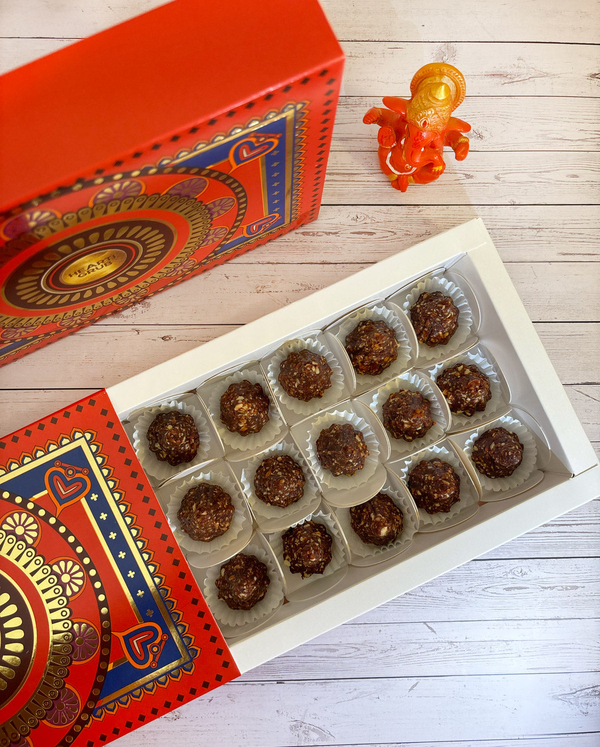 Gift set with Modak, Ganesh Chaturthi items, and a yellow ribbon on a wooden surface. Ganesh Chaturthi. Gifting. Made in Small Batches. Deliciously Decadent. Vegan Gluten Free Refined Sugar Free. Delicious Modak. Nuts. Delivery throughout U.A.E. HeartiGrub