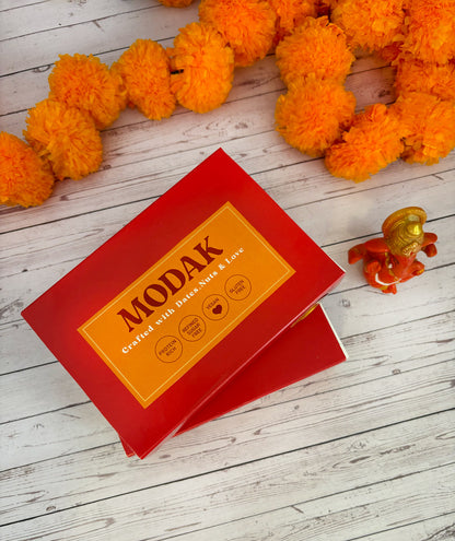 Gift set with Modak, Ganesh Chaturthi items, and a yellow ribbon on a wooden surface. Ganesh Chaturthi. Gifting. Made in Small Batches. Deliciously Decadent. Vegan Gluten Free Refined Sugar Free. Delicious Modak. Nuts. Delivery throughout U.A.E. HeartiGrub