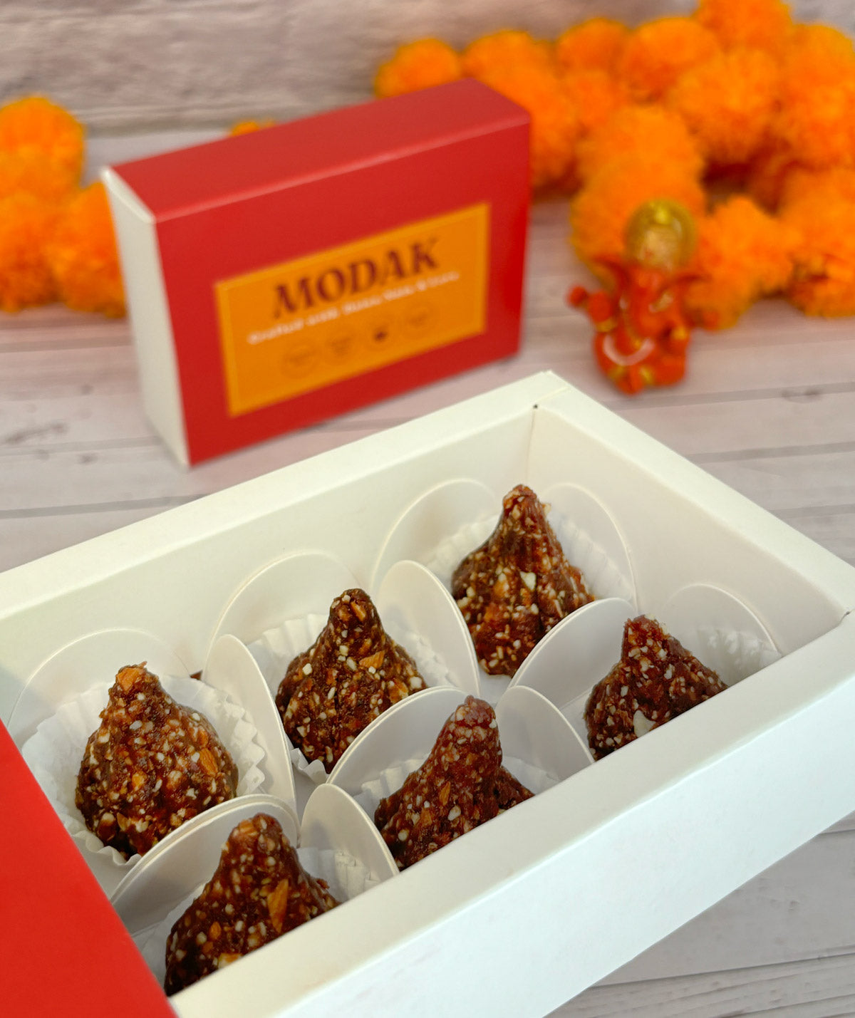 Gift set with Modak, Ganesh Chaturthi items, and a yellow ribbon on a wooden surface. Ganesh Chaturthi. Gifting. Made in Small Batches. Deliciously Decadent. Vegan Gluten Free Refined Sugar Free. Delicious Modak. Nuts. Delivery throughout U.A.E. HeartiGrub