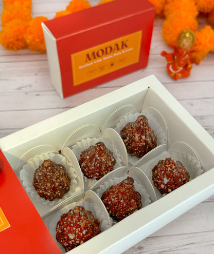 Gift set with Modak, Ganesh Chaturthi items, and a yellow ribbon on a wooden surface. Ganesh Chaturthi. Gifting. Made in Small Batches. Deliciously Decadent. Vegan Gluten Free Refined Sugar Free. Delicious Modak. Nuts. Delivery throughout U.A.E. HeartiGrub. Rose Almond Modak. Orange Cacao Hazelnut Modak