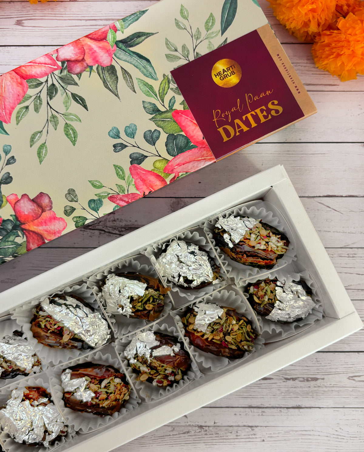 Jumbo Medjool. Royal Paan Khajur dates. No nasties. Gift set with Modak, Ganesh Chaturthi items, and a yellow ribbon on a wooden surface. Ganesh Chaturthi. Gifting. Made in Small Batches. Deliciously Decadent. Vegan Gluten Free Refined Sugar Free. Delicious Modak. Nuts. Delivery throughout U.A.E.