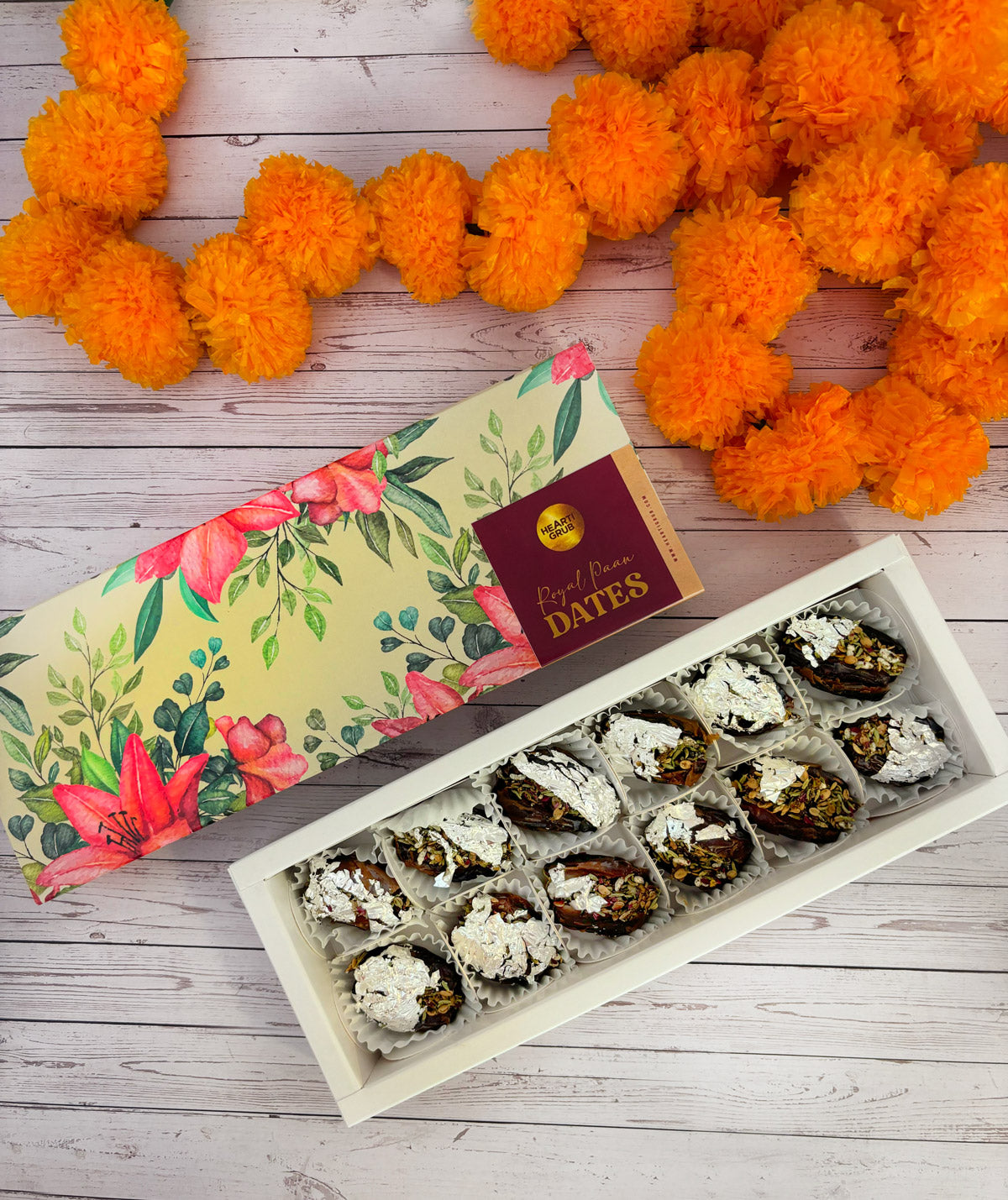 Jumbo Medjool. Royal Paan Khajur dates. No nasties. Gift set with Modak, Ganesh Chaturthi items, and a yellow ribbon on a wooden surface. Ganesh Chaturthi. Gifting. Made in Small Batches. Deliciously Decadent. Vegan Gluten Free Refined Sugar Free. Delicious Modak. Nuts. Delivery throughout U.A.E.