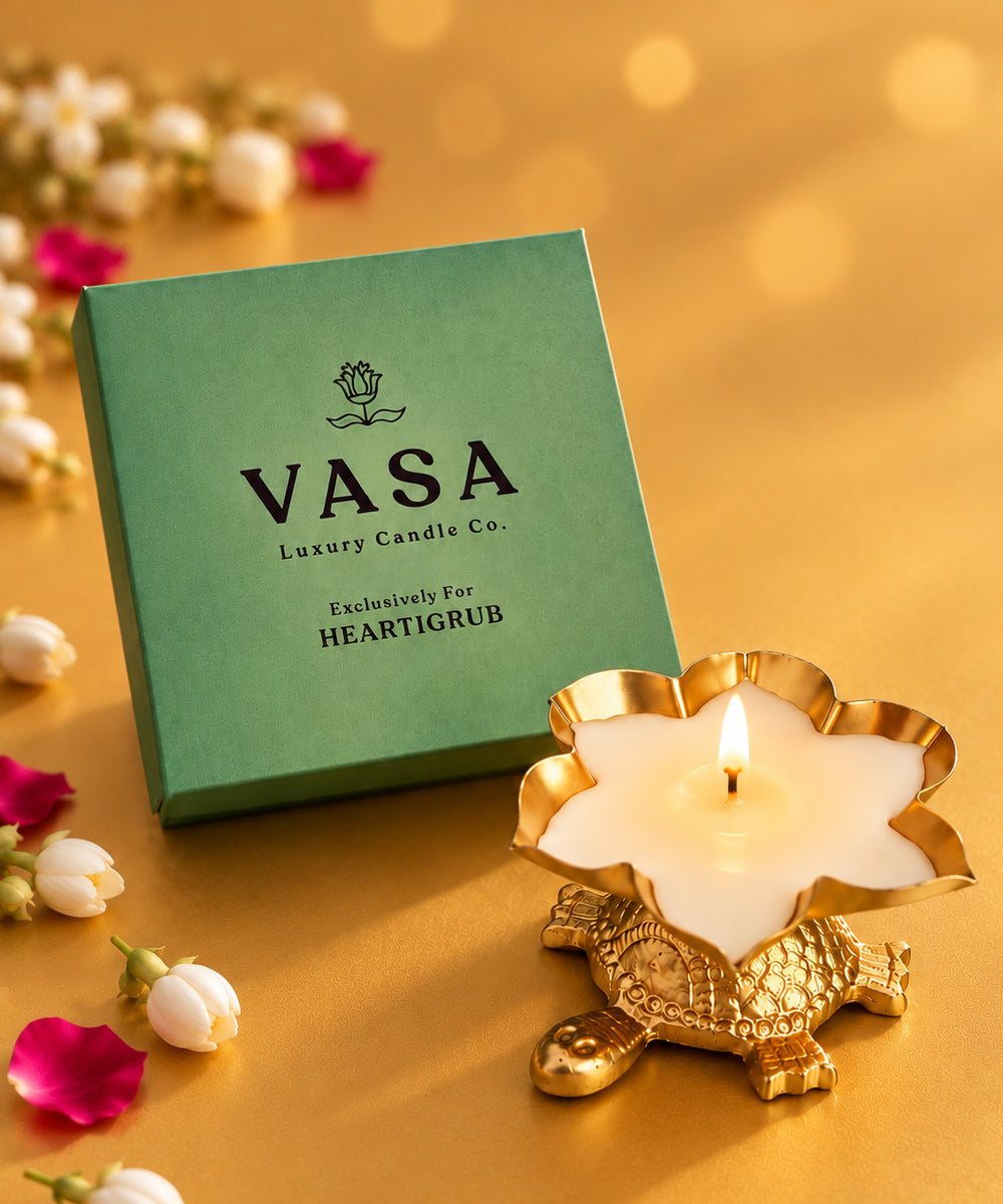 A VASA Luxury Candle Co. 'Heartigrub' candle in a gold turtle-shaped holder, shown next to its green packaging box on a warm gold background with decorative white and pink flowers. Diwali gifts Dubai, luxury Diwali gifts UAE, Diwali candle gift, festive gift add-ons, premium Diwali hampers Dubai, corporate Diwali gifting UAE. Heartigrub. Sustainable Gifts